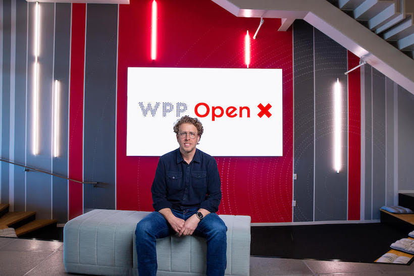 Andrew Keller full body shot in front of theb WPP aqnd Open X logos